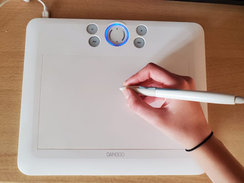 a woman's hand drawing with a stylus on a white coloured graphics tablet