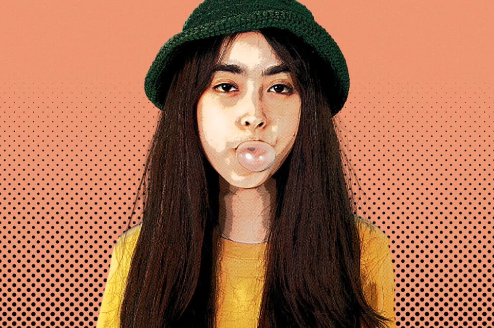 Woman blowing a bubblegum bubble, with a halftone effect, wearing a green hat